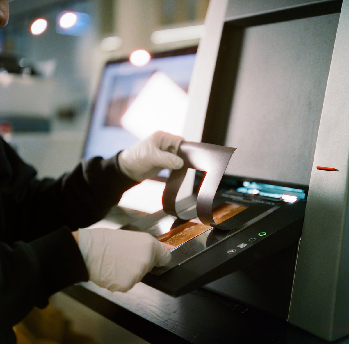 A gloved hand loading film into a scanner at IROHAS Photo